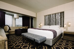 A hotel room with a large bed, a sofa, a bench, and a wall-mounted TV.
