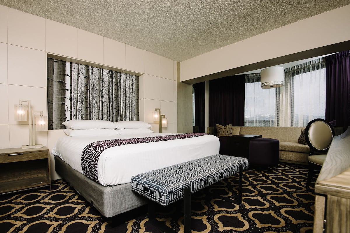 A hotel room with a large bed, a bench, a sofa, and a desk.