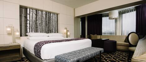 A hotel room with a large bed, a bench, a sofa, and a desk.
