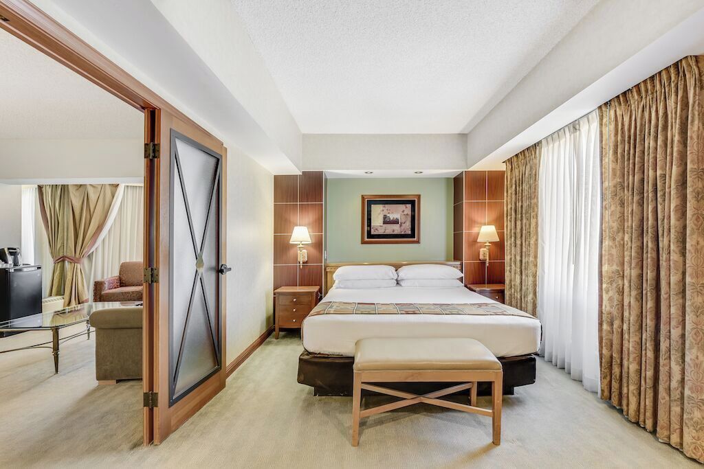Una habitación de hotel con una cama, mesitas de noche, un banco, un escritorio y una silla.