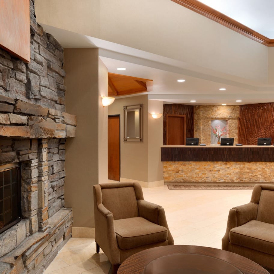 A lobby with a stone fireplace, two armchairs, a reception desk, and a wooden ceiling.