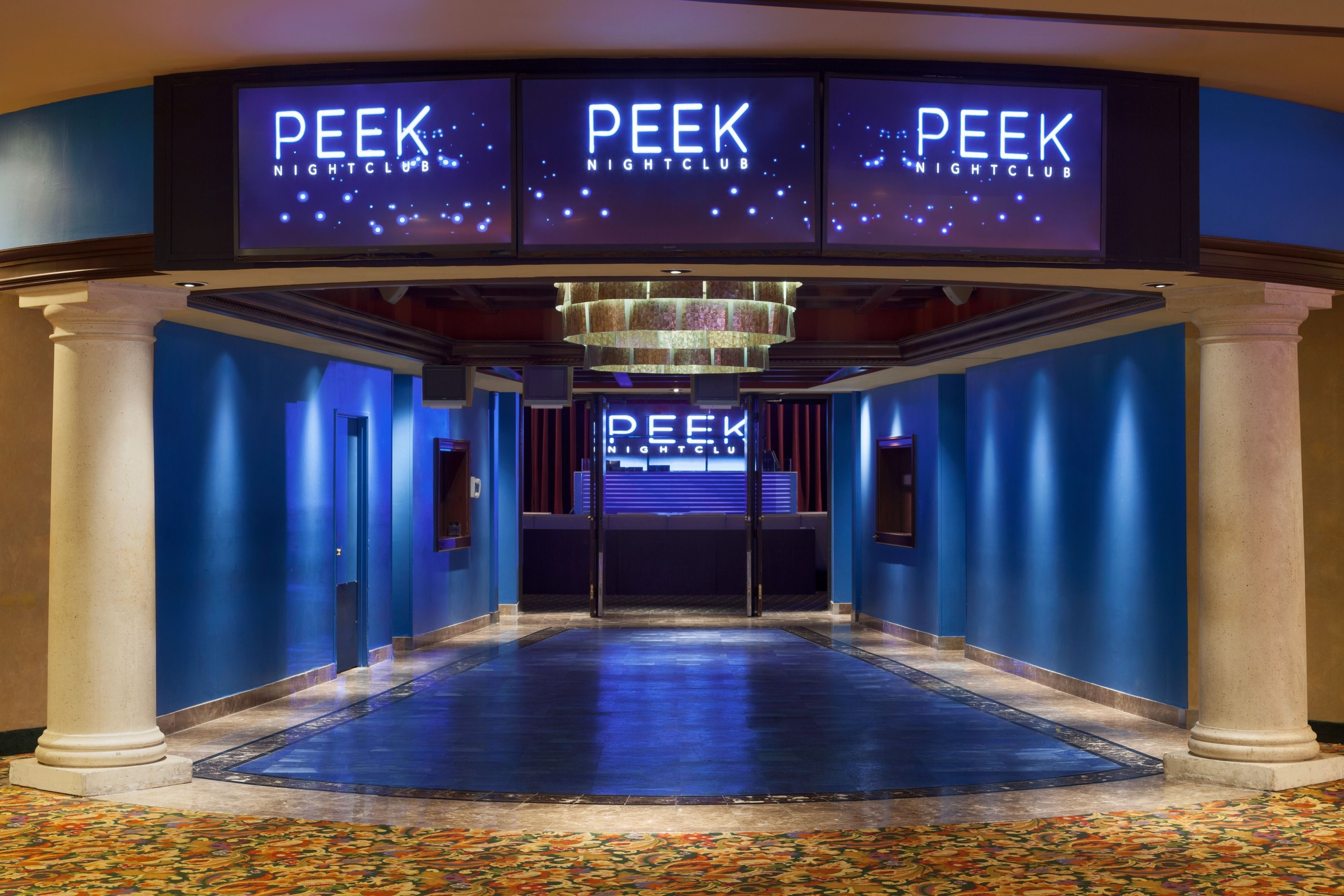 A hallway with a blue carpet, a chandelier, and columns.