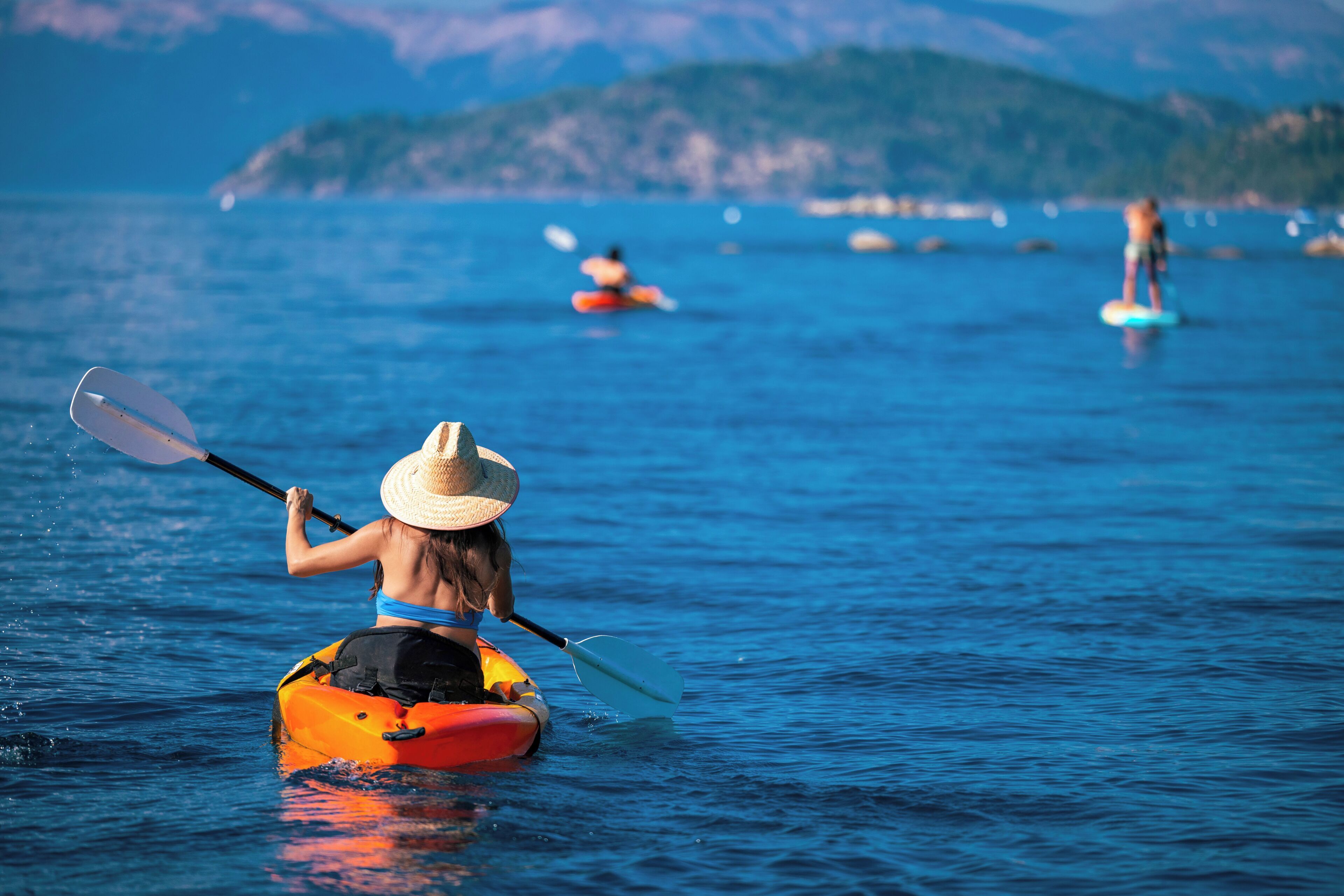Una persona practica kayak en aguas tranquilas, con un paisaje montañoso al fondo.