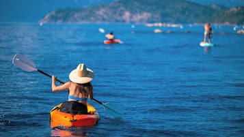 Una persona practica kayak en aguas tranquilas, con un paisaje montañoso al fondo.