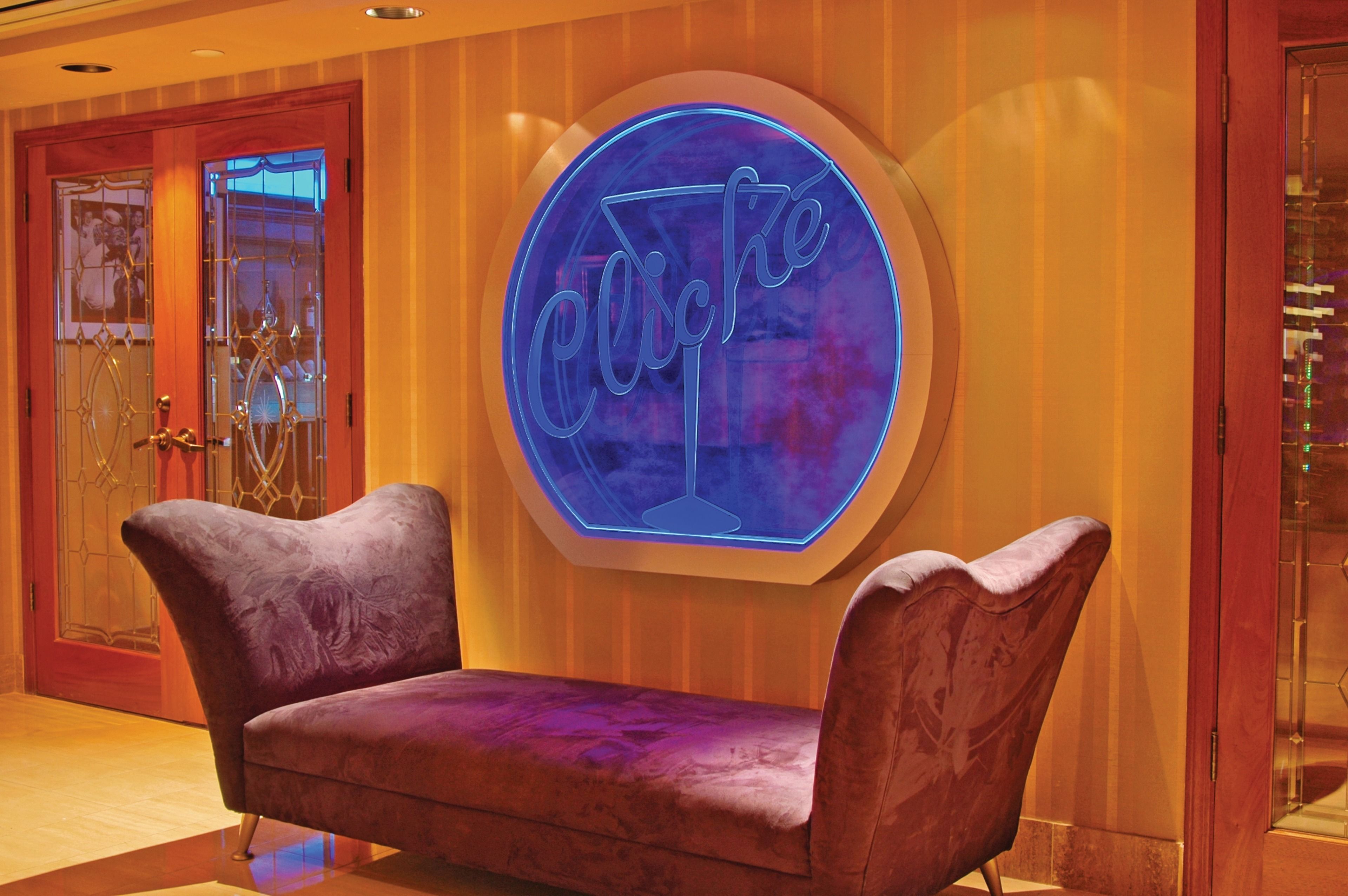 A room with a purple velvet sofa, a neon sign with the word "Cliché," and a wooden door with glass panels.