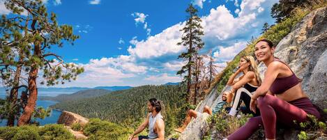 Un grupo de personas sentadas sobre rocas, con un paisaje montañoso y un lago al fondo.