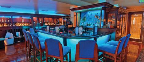 A bar area with a glass counter, multiple bar stools, and a well-stocked bar.