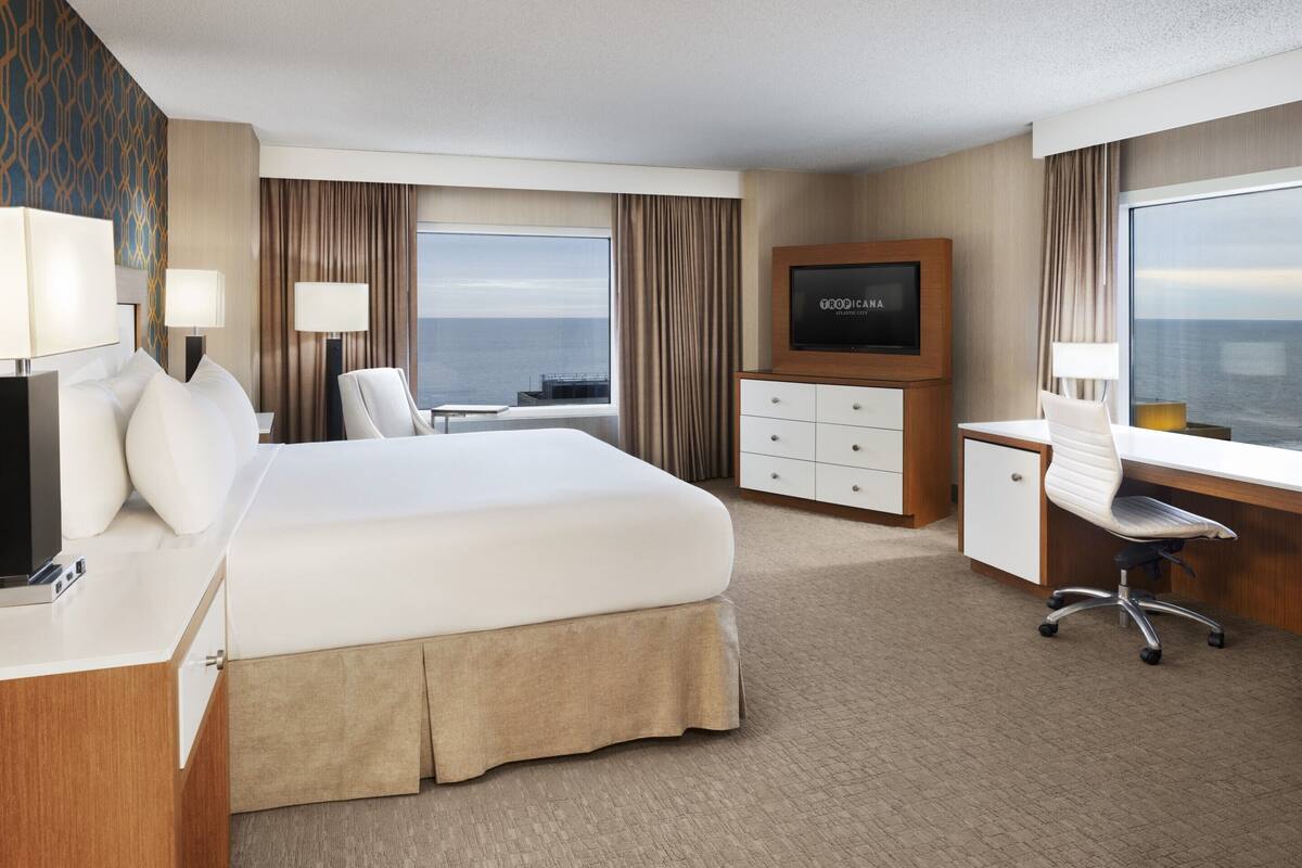 Ett hotellrum med en stor säng, ett skrivbord, en tv och utsikt över havet.