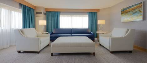 A hotel room with a large bed, two armchairs, a sofa, and a small table with lamps.