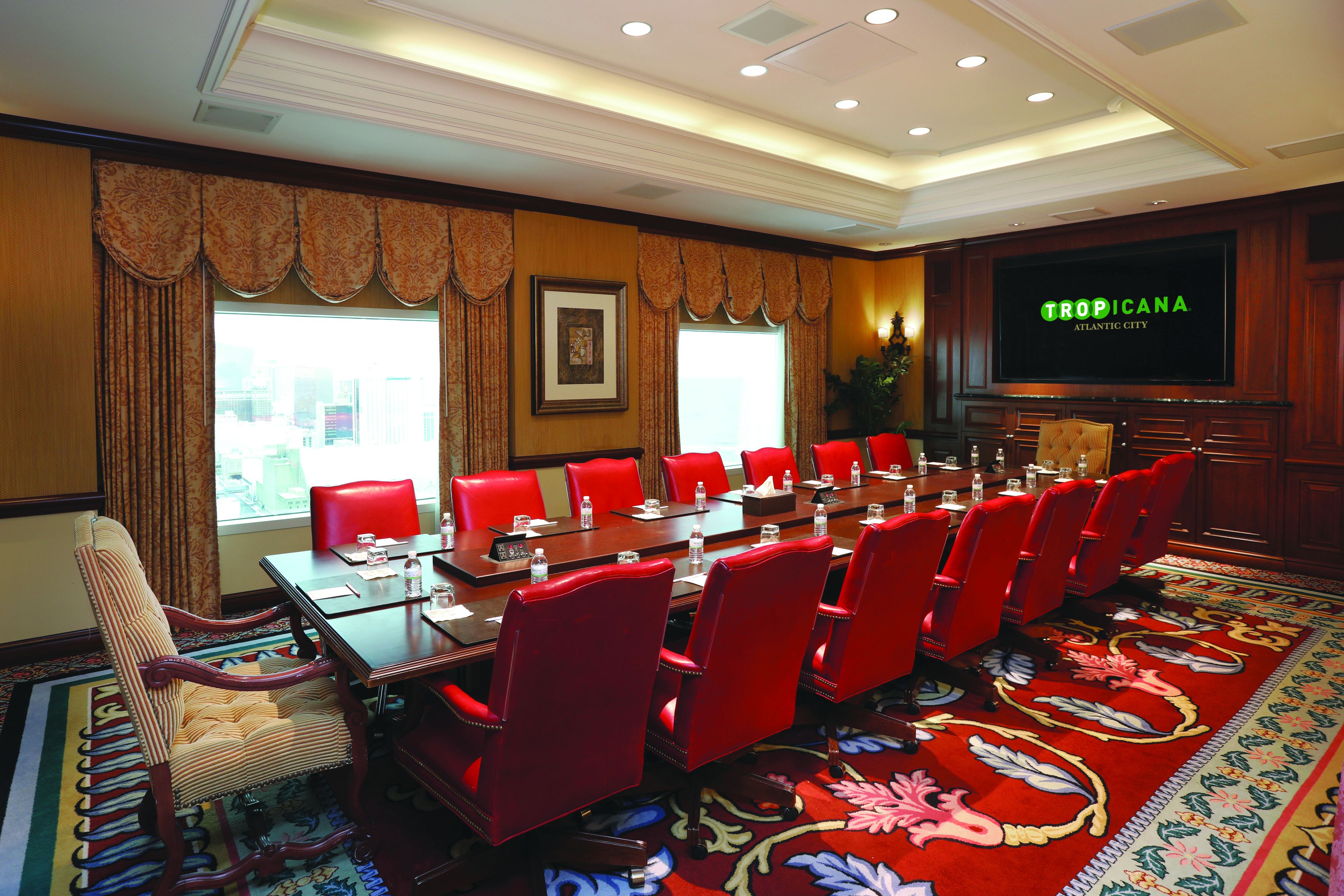 A conference room with a long table, red chairs, and a large screen displaying "TROPICANA ATLANTIC CITY".