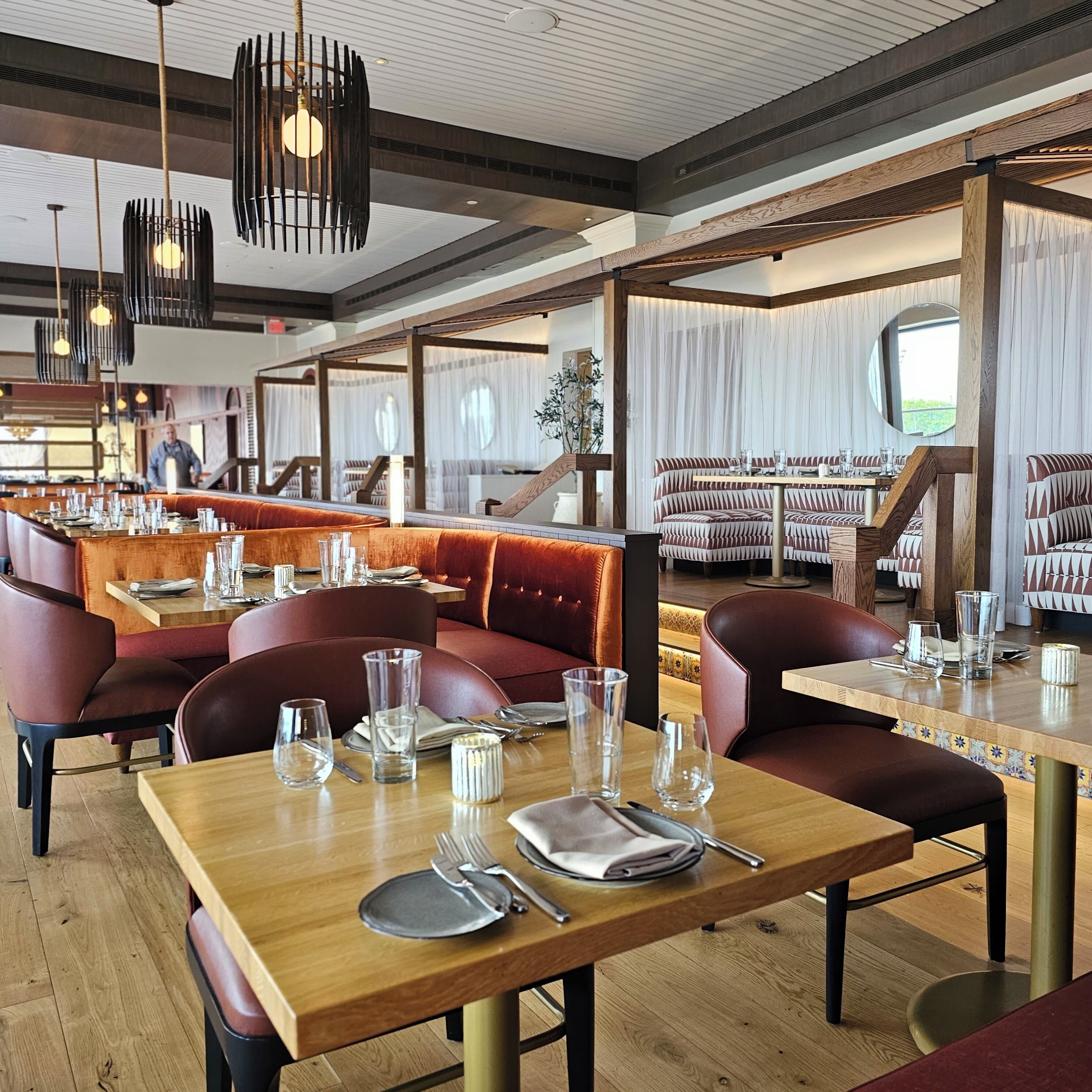 A restaurant with wooden tables, leather booths, and hanging pendant lights.