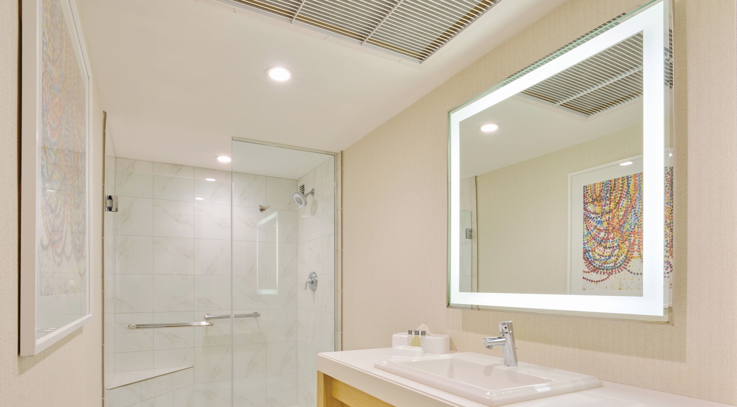 A modern bathroom with a glass-enclosed shower, a large mirror, and a white sink.