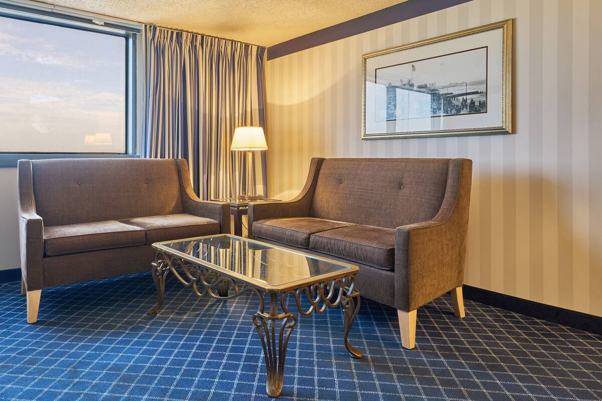 Ett hotellrum med en soffgrupp, ett soffbord i glas och en lampa.