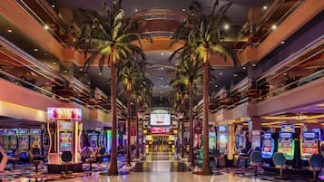 A multi-level indoor space with arcade gaming machines, palm trees, and a central escalator.