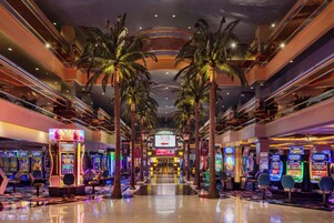 Un espacio interior de varios niveles con máquinas de juegos de arcade, palmeras y una escalera mecánica central.