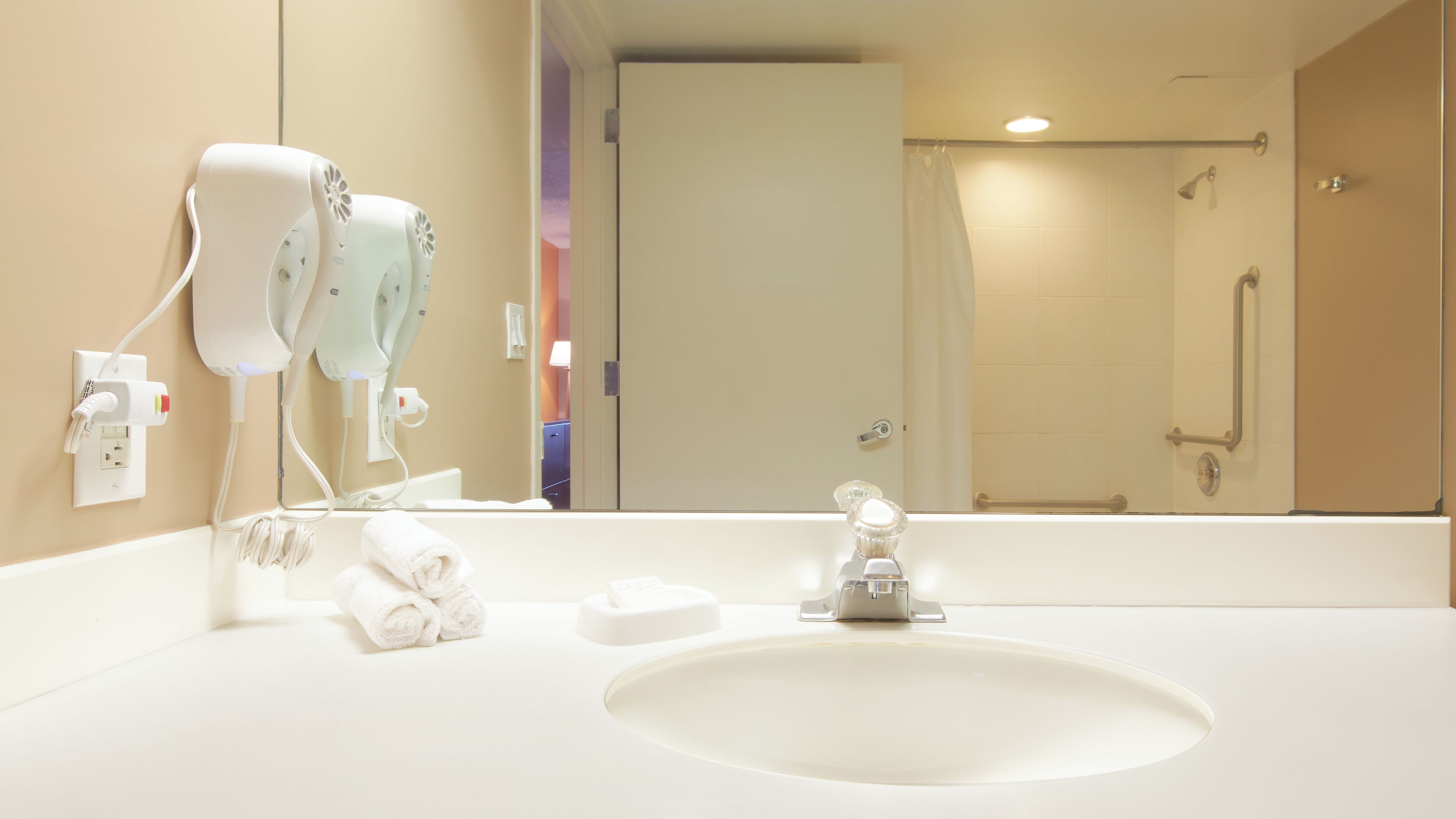 Une salle de bain d’hôtel avec un lavabo blanc, un miroir, une serviette et un espace douche.