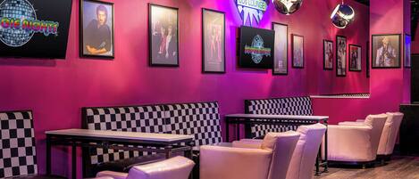 A lounge area with checkered booths, framed posters on the wall, and a neon sign.
