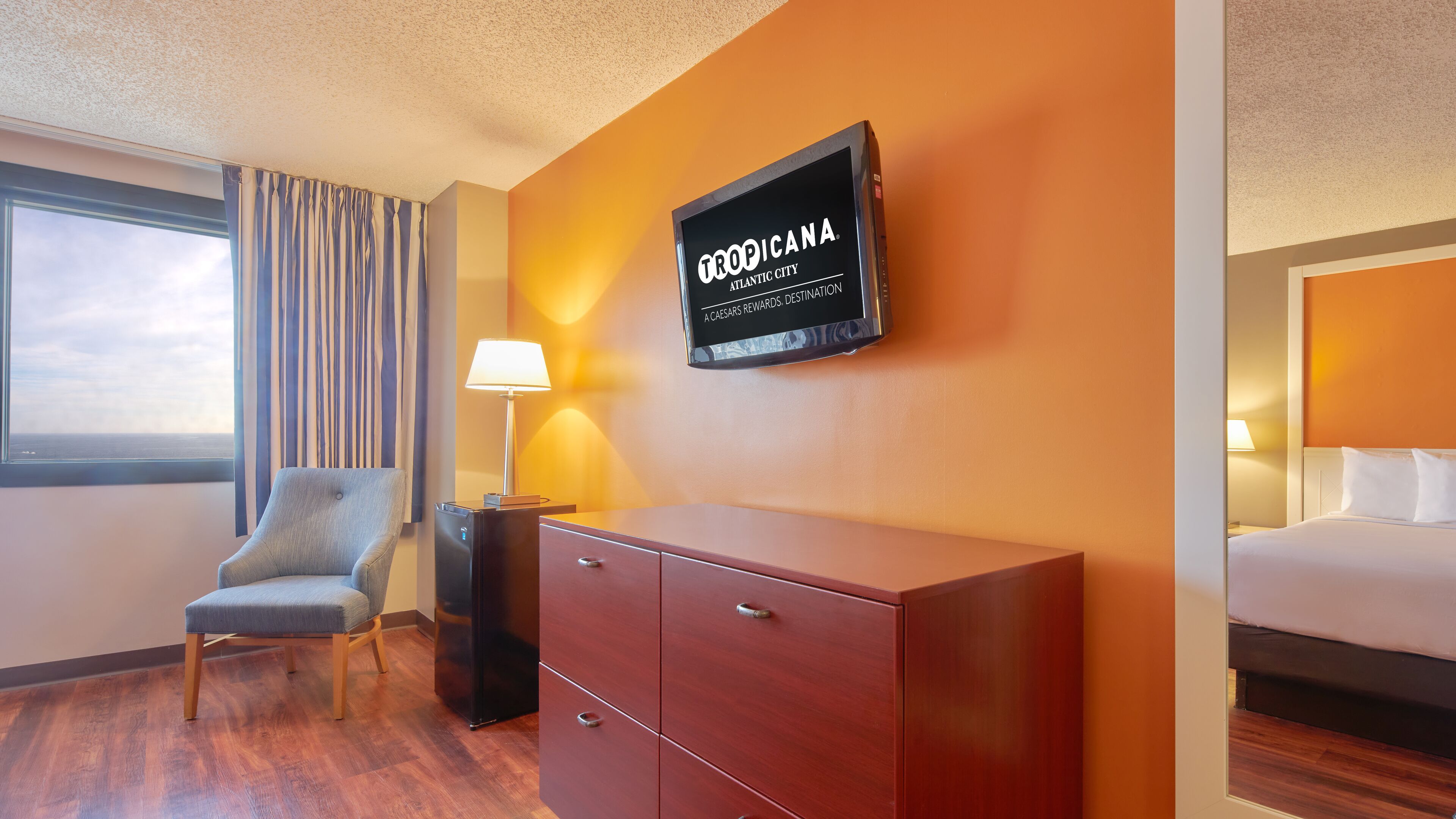 Habitación de hotel con cama, escritorio, silla, televisor montado en la pared y ventana con cortinas.
