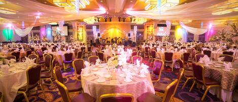 A banquet hall with round tables set for a formal event, featuring a stage at the front and a large audience seated.