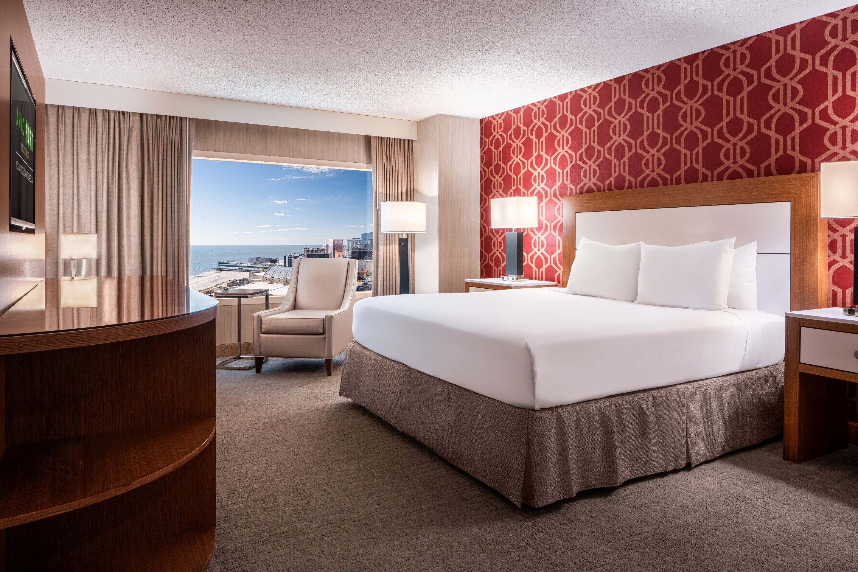 A hotel room with a large bed, a desk, a chair, and a view of the city and ocean.