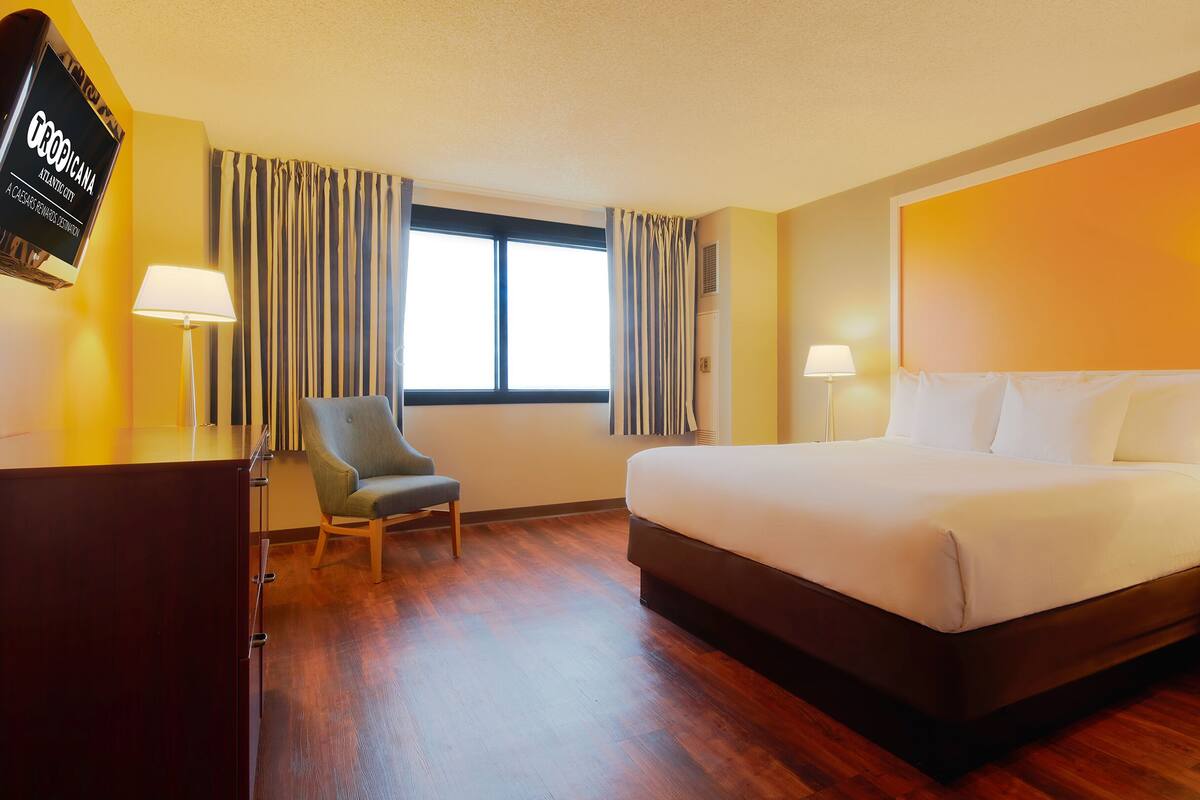 Ett hotellrum med en stor säng, en stol, ett skrivbord och en tv som visar programmet ”Atlantica Atlantic City”.