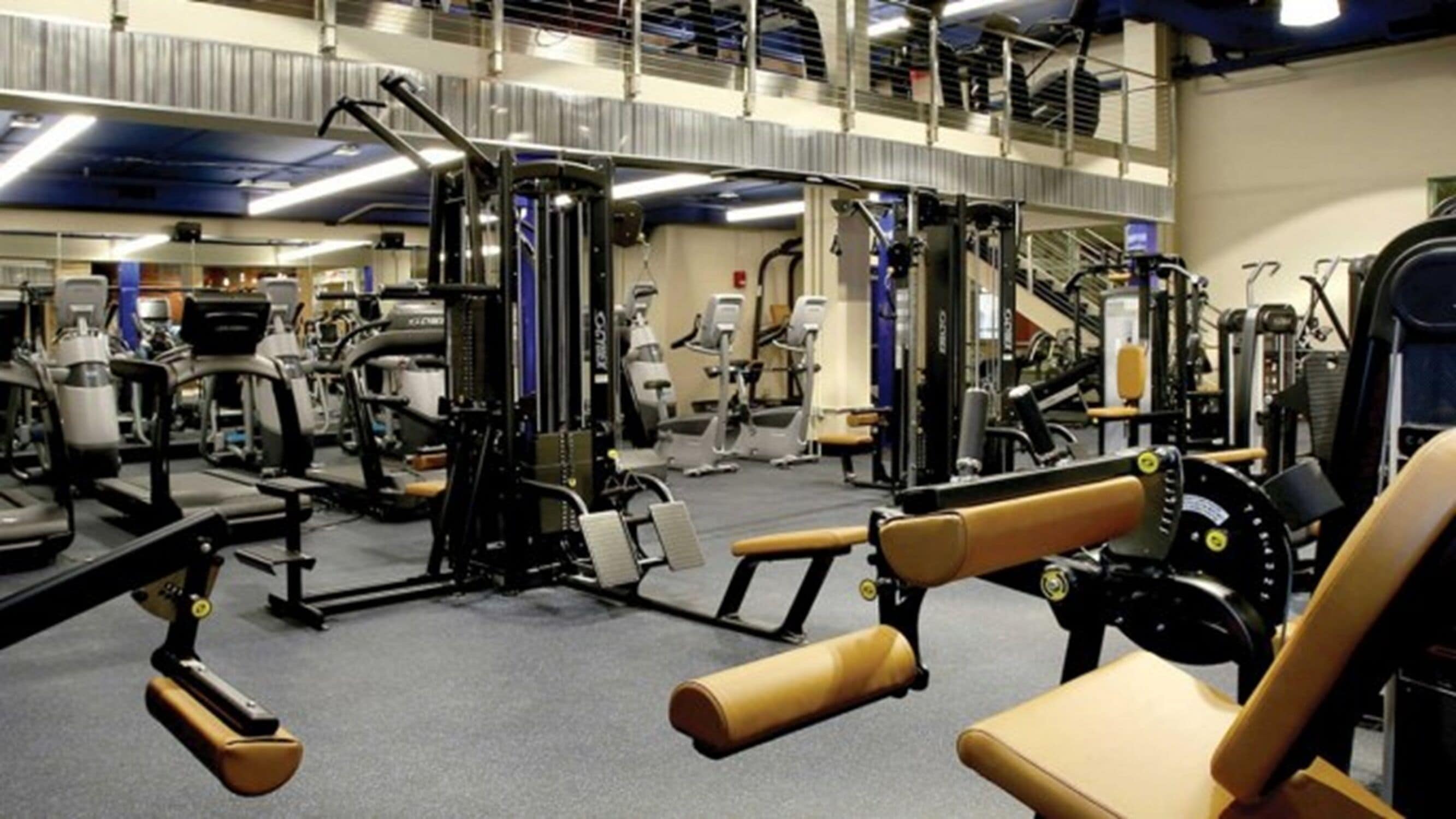 A gym with various exercise machines, a large mirror, and a mezzanine level.