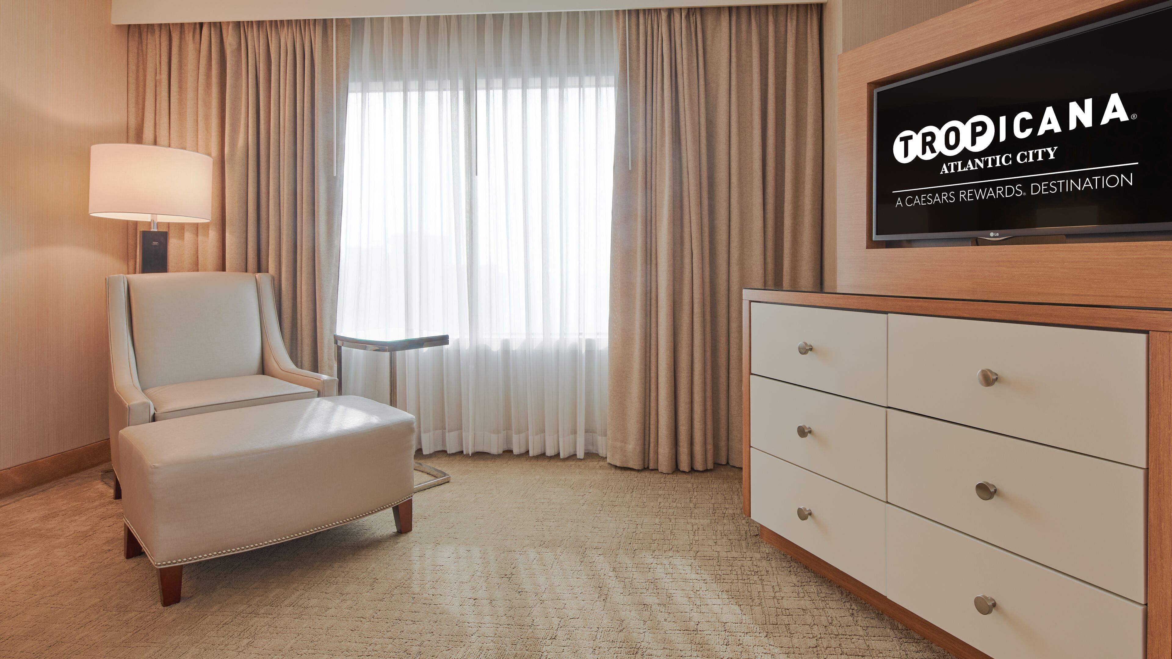 A hotel room with a large window, a chair, a TV, and a dresser.
