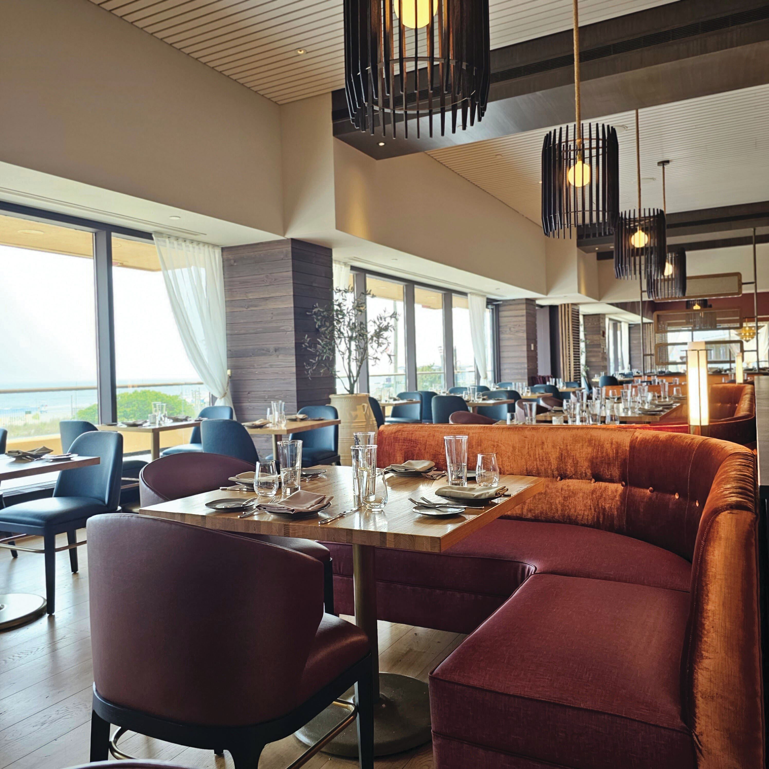 A modern restaurant with high ceilings, large windows, and a mix of seating options including booths and tables.