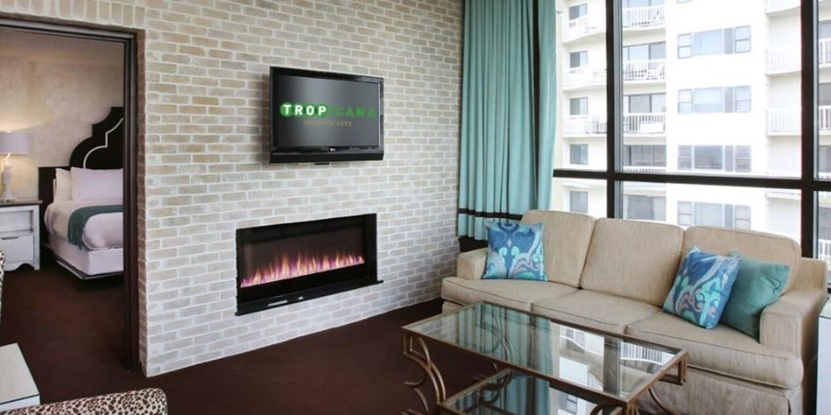 A modern living room with a fireplace, a television mounted on the wall, a sofa with cushions, and a glass coffee table.