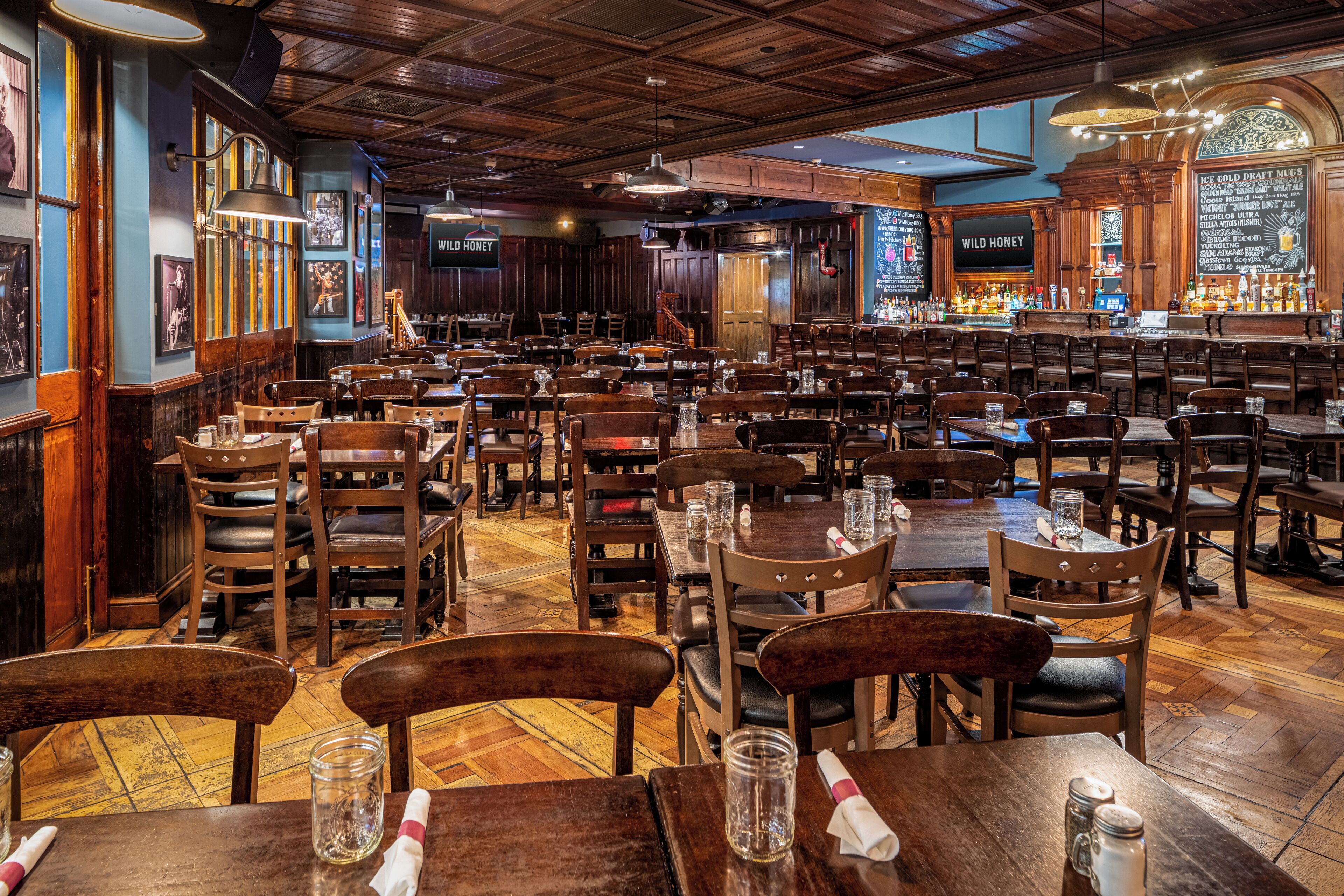 A spacious restaurant with wooden tables and chairs, a bar area, and a chalkboard menu.