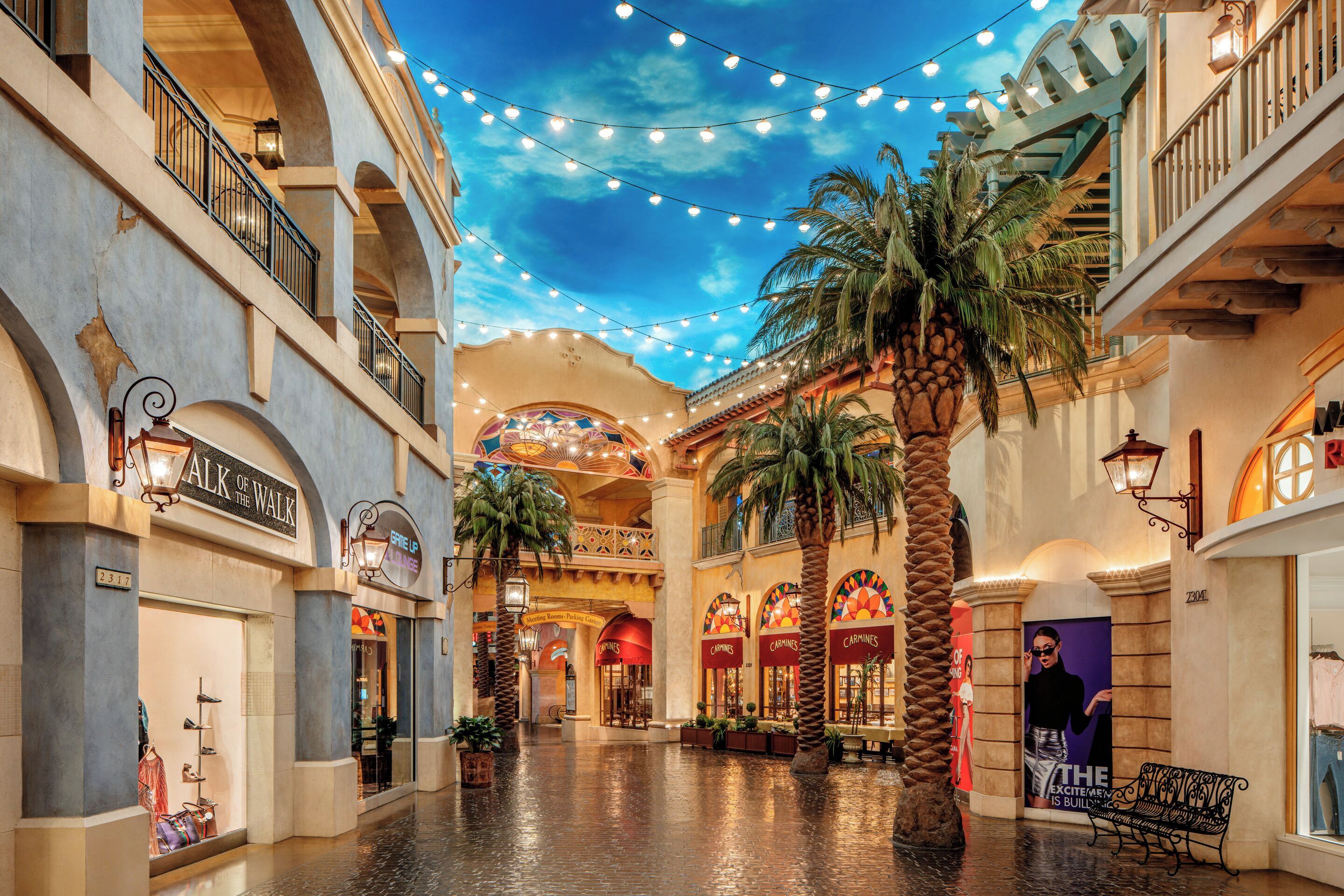 A shopping mall with multiple levels, palm trees, and string lights.