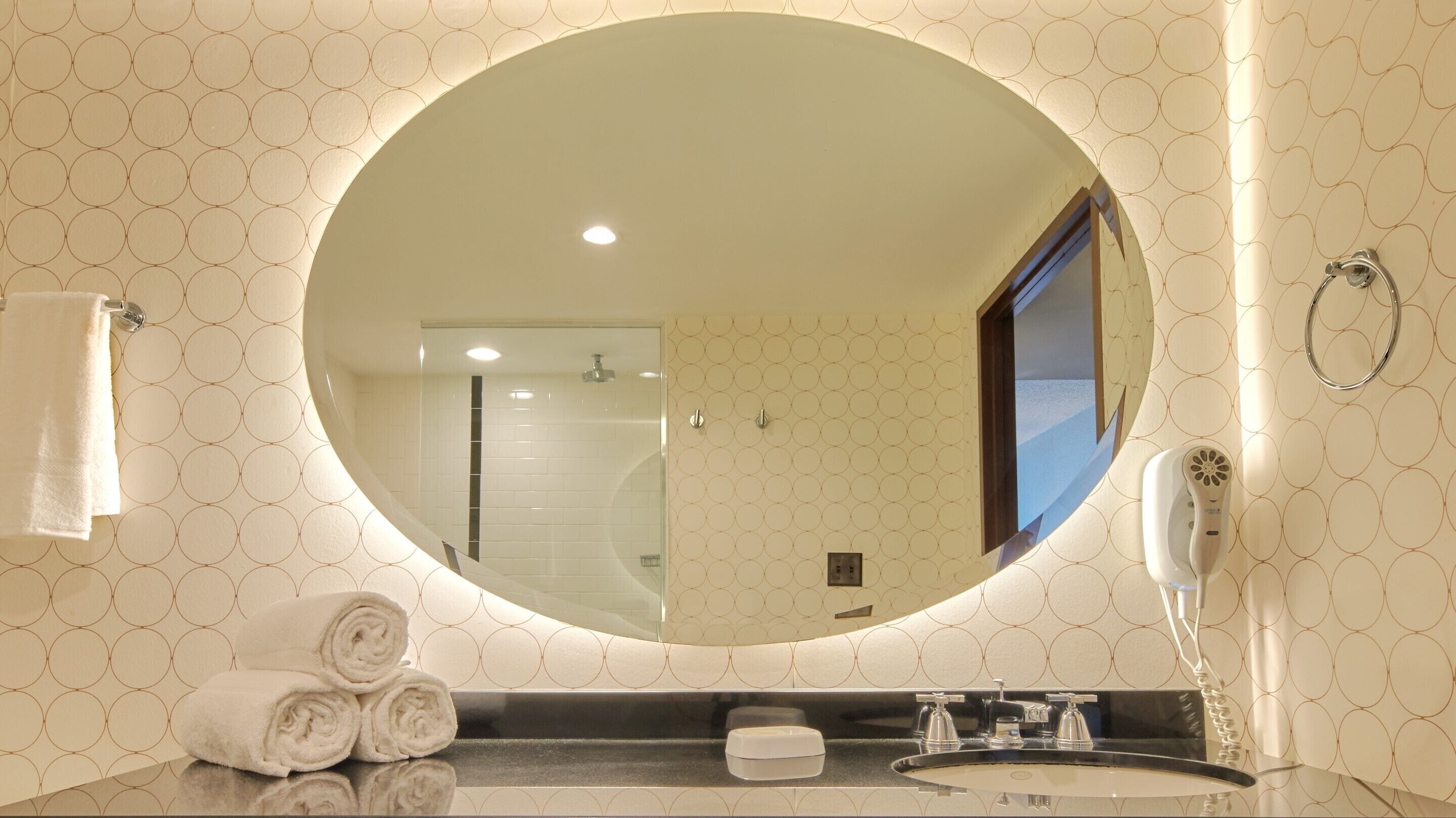 A bathroom with a large mirror, a towel rack, a hairdryer, and a sink.