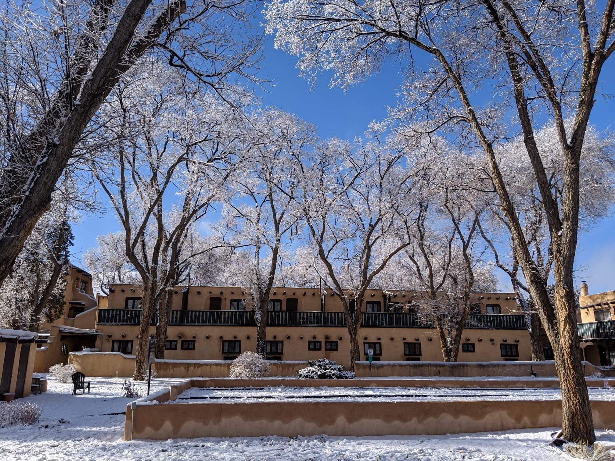 A courtyard with snow-covered trees and a building with balconies.