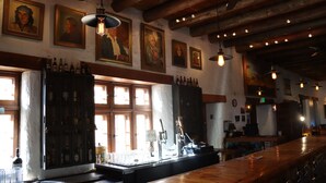 A bar area with wooden beams, framed portraits on the wall, and a bar counter with bottles and glasses. - Sagebrush Inn & Suites (Taos)