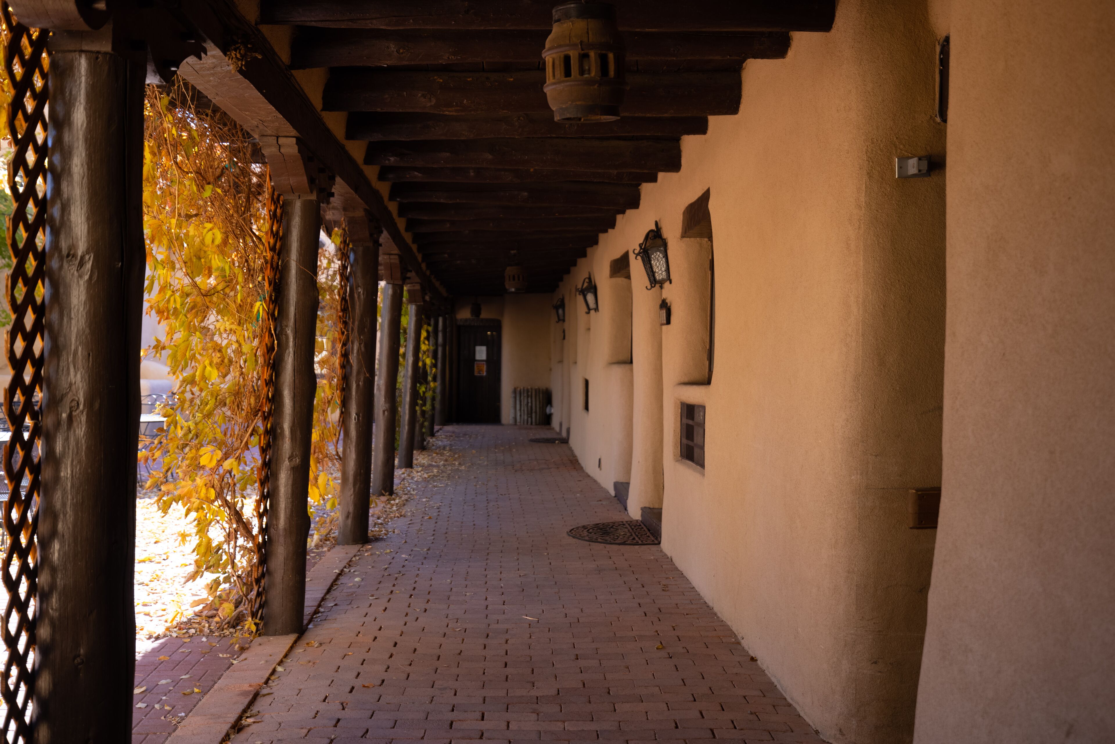 A corridor with brick flooring, wooden columns, and hanging lanterns.