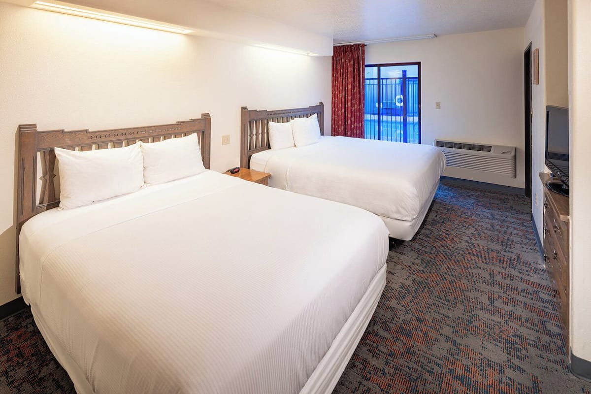 A hotel room with two beds, a TV, and a view of a pool through a window.