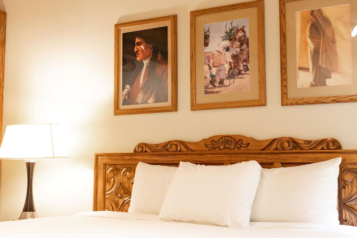 A hotel room with a wooden headboard, a bed with white linens, and three framed pictures on the wall.