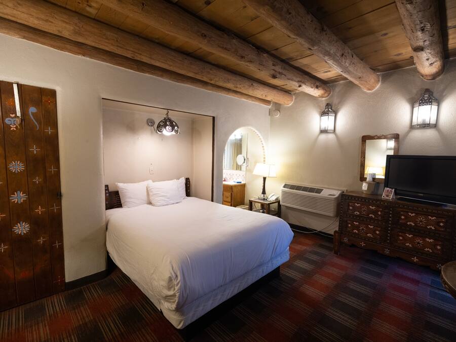 Et hotelværelse med en stor seng, træbjælker i loftet, et fladskærms-tv, en kommode og et mønstret tæppe.