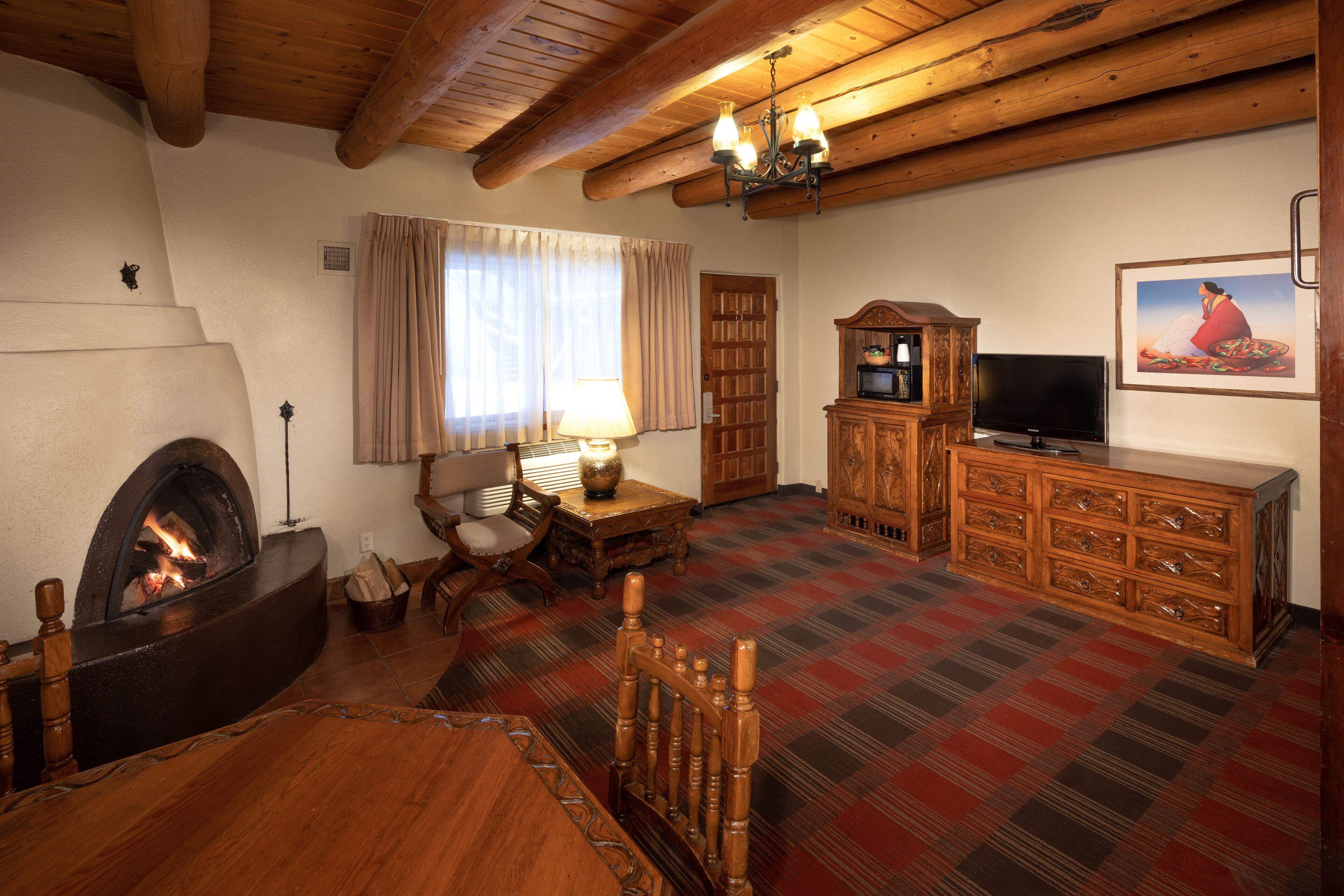 A cozy living room with a fireplace, wooden furniture, a television, and a plaid carpet.