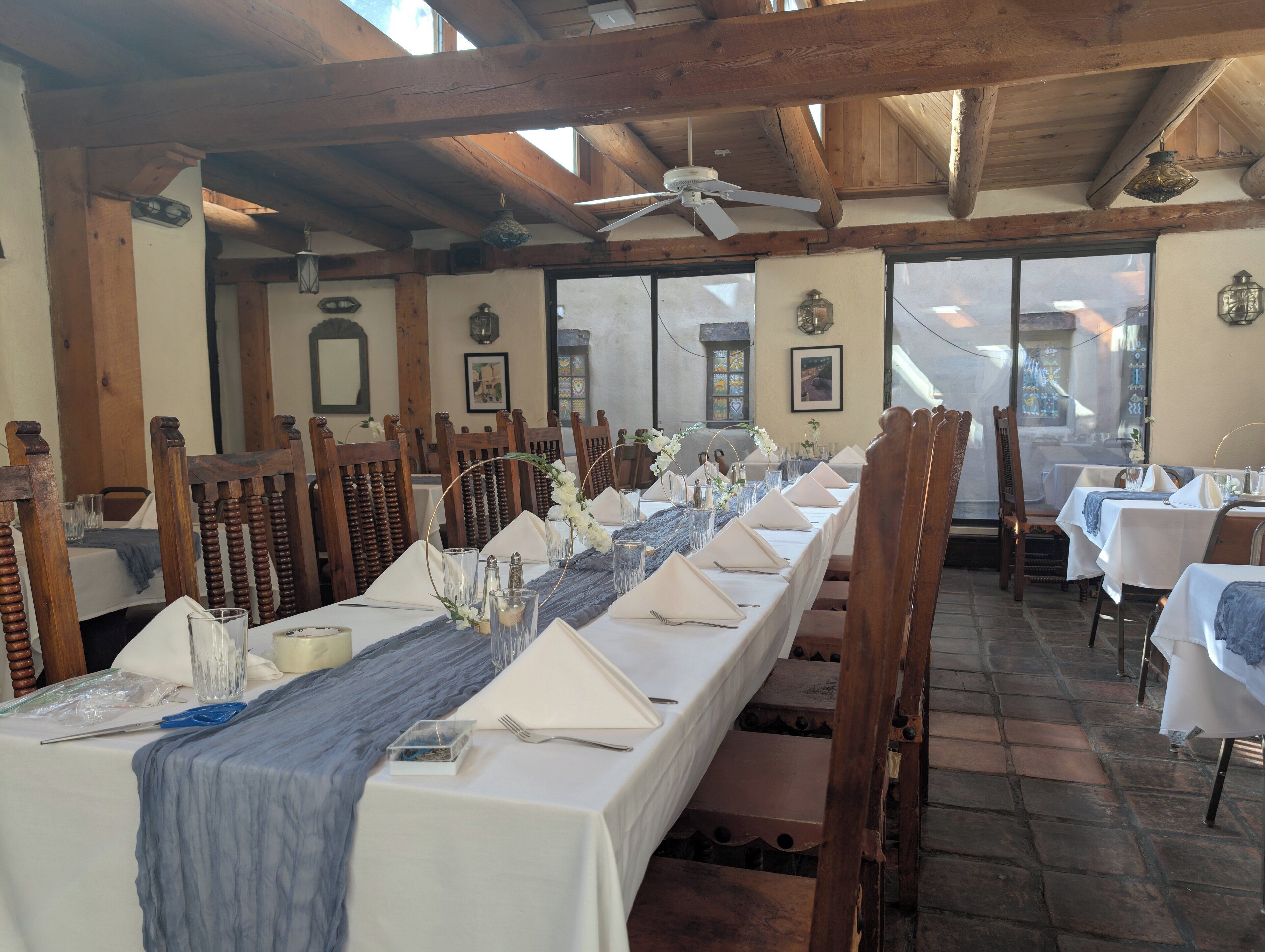 A long dining table set with white tablecloths, wooden chairs, and a blue runner.