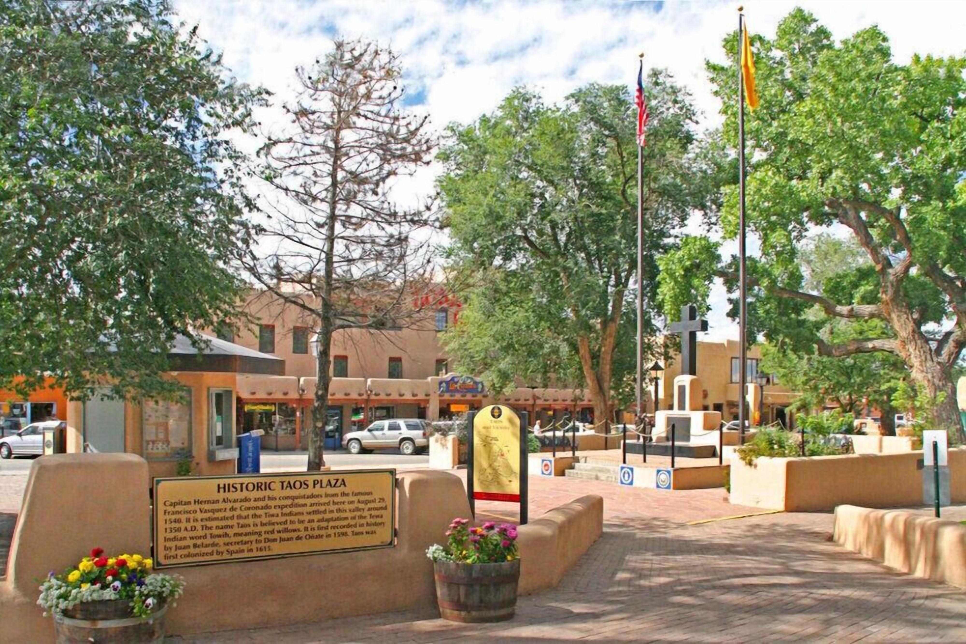 A historic plaza with a sign, a flag, and a building in the background.