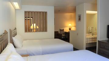 A hotel room with two beds, a desk, a chair, and a bathroom visible through an open door.