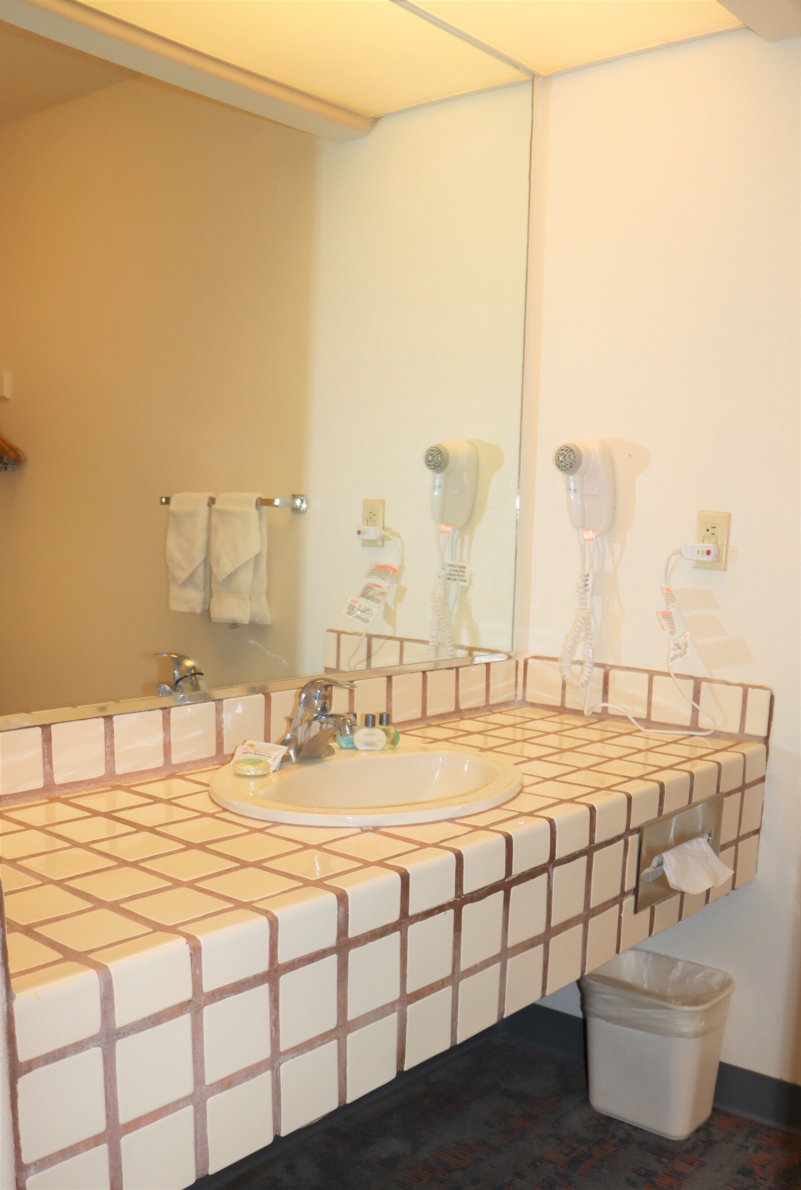 Un baño con lavamanos, espejo, toallero y dos secadores de pelo.