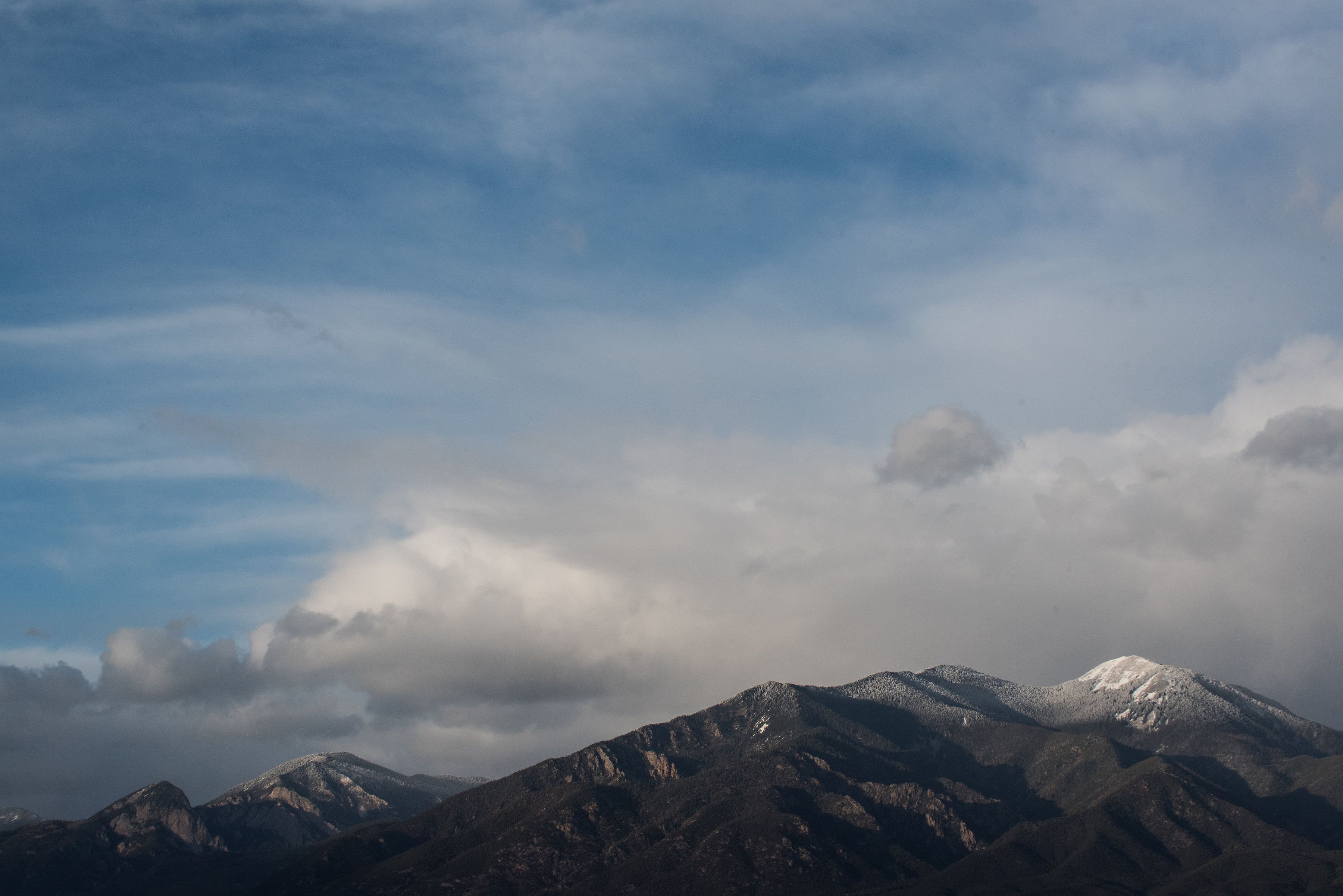 Une chaîne de montagnes aux sommets enneigés, sous un ciel nuageux.