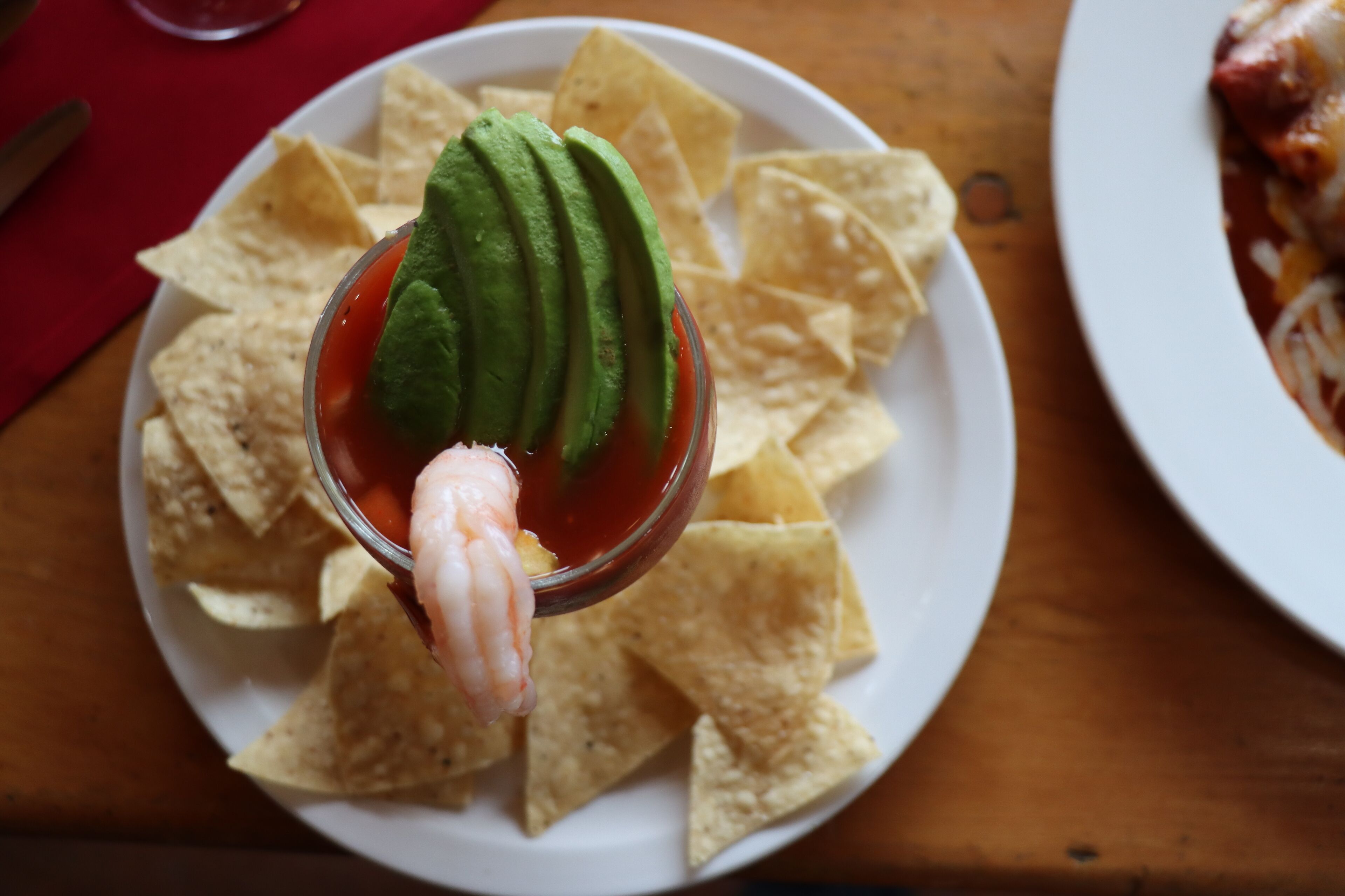 Un plato de totopos de maíz con un vaso de una bebida roja y una porción de aguacate.