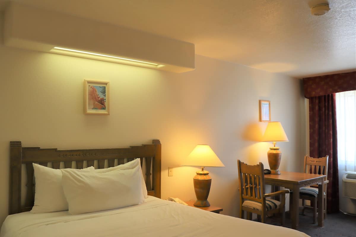 A hotel room with a bed, two bedside lamps, a table with chairs, and a picture on the wall.