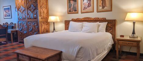 A hotel room with a large bed, two bedside tables with lamps, a wooden bench, a wooden wardrobe, and three framed pictures on the wall.