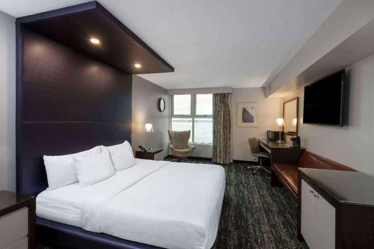 Une chambre d’hôtel avec un lit, un bureau, une chaise, une télévision et une fenêtre avec des rideaux.