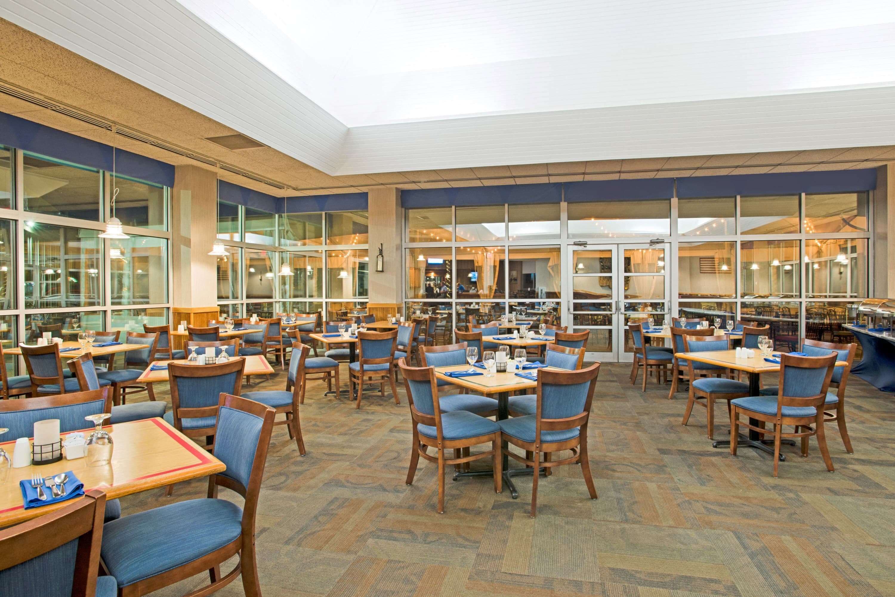 A spacious dining area with multiple tables and chairs, large windows, and a high ceiling.