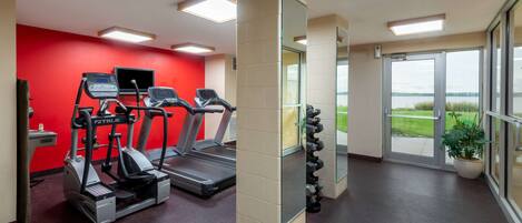 Un gimnasio con cintas de correr, una pared roja y un amplio ventanal con vistas.